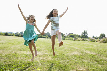 Two girls running and jumping hand in hand through field