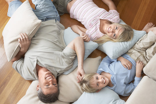 Portrait of happy family of three lying on floor with cushions at home