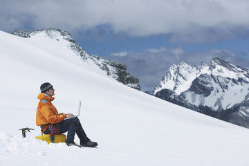 Fototapeta na wymiar Side view of a male hiker using laptop on snowy mountain slope