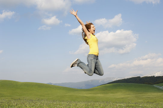 Side view of young woman with arms raised screaming while jumping in park