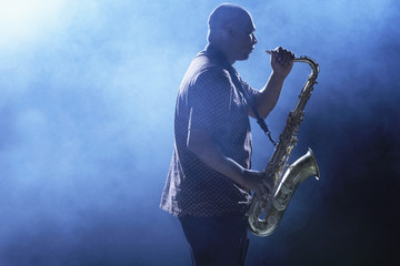 Fototapeta na wymiar Side view of an African American man playing saxophone against smoky background