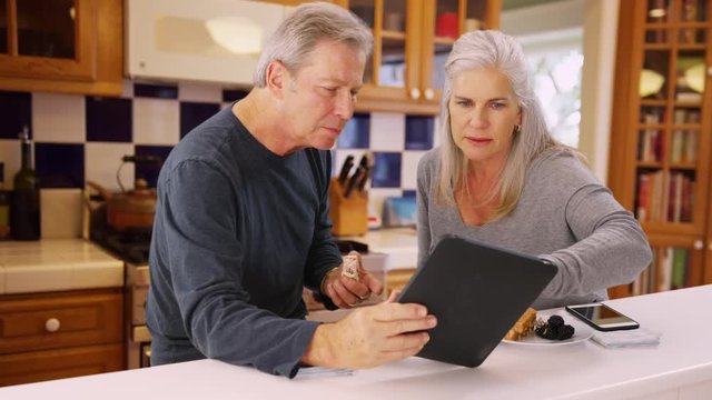 Charming mature white couple looking at handheld tech while eating lunch