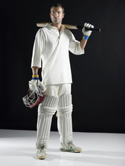 Full length of a cricket player holding bat on shoulder against black background © MDBPIXS