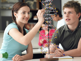 Happy teenage students examining DNA model and taking notes in science class