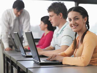 Fototapeta premium Portrait of teenage girl with classmates using laptops in computer class
