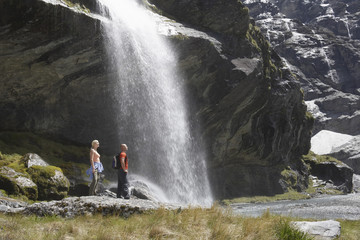 Full length side view of two hikers standing by waterfall at river