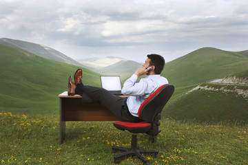Rear view of businessman using  cell phone at desk in mountain field