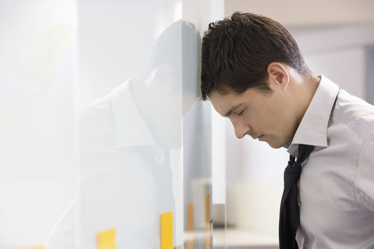 Side view of an unhappy businessman resting head against office wall 