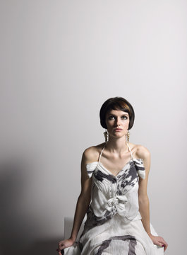 Serious young woman in dress sitting against gray background