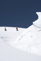 Side view of two hikers walking past ice formation at a distance in snowy mountains