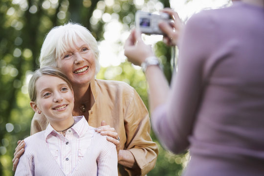 Woman photographing grandmother and granddaughter through digital camera in park