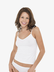 Portrait of a young smiling woman in camisole and knickers against white background