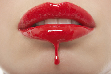 Detail shop of red lipgloss dripping from woman's lips