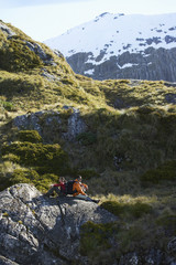 Side view of two hikers sitting on boulders in mountain valley
