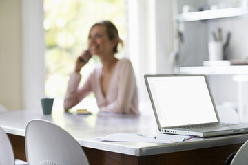 Young woman using mobile phone with laptop and documents in foreground