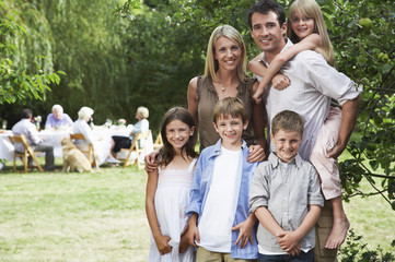 Portrait of happy parents and children in garden with family in background