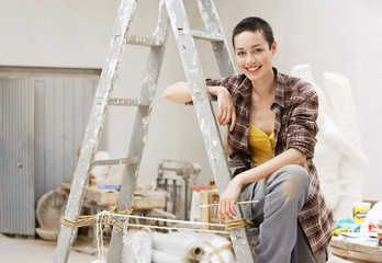 Portrait of happy young female painter sitting on ladder at work site