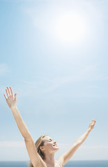 Smiling young woman with arms raised at beach on sunny day