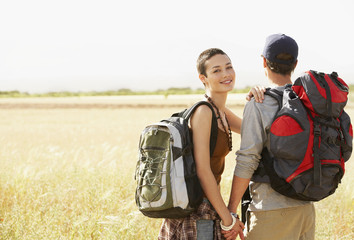Happy hiking couple with backpacks holding hands in field