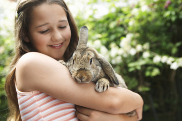 Happy young girl holding bunny rabbit in the backyard - Powered by Adobe