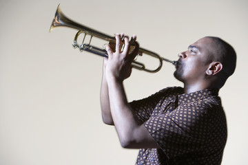 Side view of an African American man playing trumpet against gray background - obrazy, fototapety, plakaty