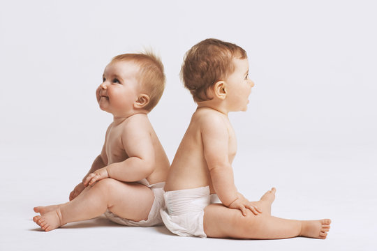 Side view of babies sitting back to back on white background