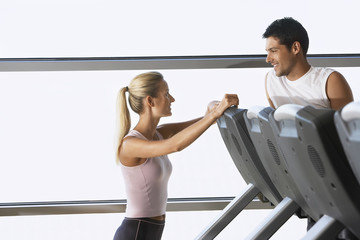 Female trainer conversing with man on treadmill at gym