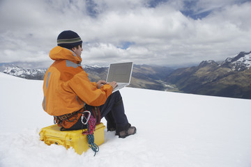 Fototapeta na wymiar View of a male hiker using laptop on snowy mountain landscape