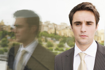 Confident young businessman looking away while standing by glass wall