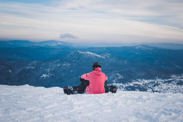 Fototapeta na wymiar Sportsman snowboarder sits and prepares for descent from snow to