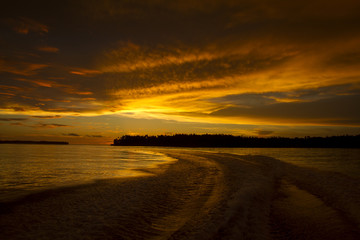 Fototapeta na wymiar Golden light raze hit clouds over island at dusk