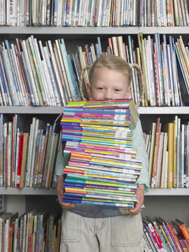 Portrait of young little girl carrying stack of books in library