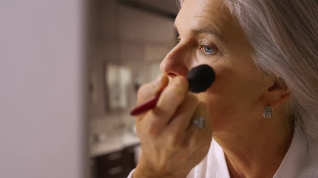 Attractive mid aged woman applying blush makeup