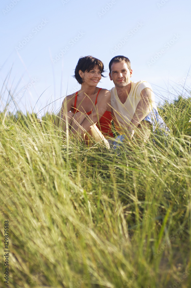 Wall mural Young romantic couple sitting in tall grass at beach