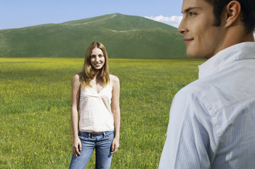 Happy teenage girl looking at boyfriend while standing in field