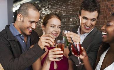 Two happy multiethnic couples toasting drinks at the bar
