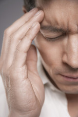 Fototapeta premium Detail of a male executive with fingers pressed to forehead against gray background