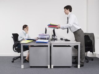 Side view of a businessman passing folders to female colleague across the desk