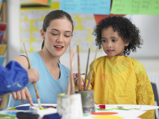 Young teacher assisting cute girl in painting during art class