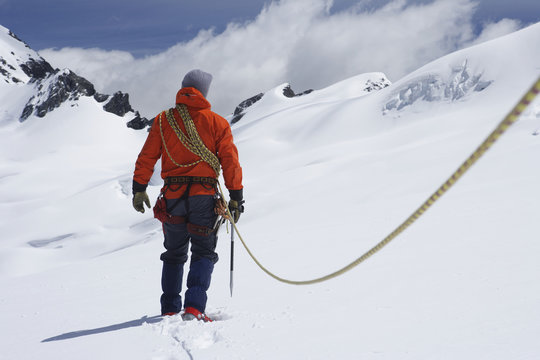 Rear view of a male hiker connected to safety line in snowy mountains