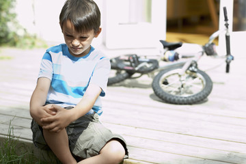 Sad little boy sitting on porch of house with bicycle in background