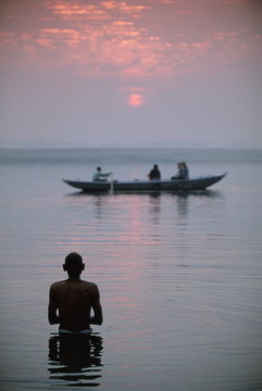 Boat passing a man standing in the holy river , River Ganges (Ganga), Varanasi (Benares), Uttar Pradesh state