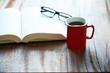 A cup of coffee with book and glasses on wooden table. Enjoy reading.