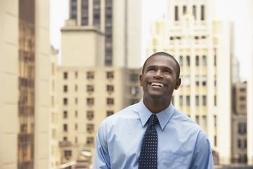 Fototapeta premium Happy African American businessman looking up against office buildings