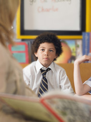 Elementary schoolboy listening to teacher reading in classroom