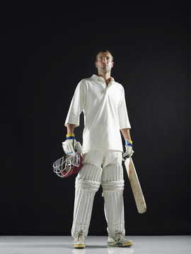 Full Length Of A Cricket Player Holding Bat And Helmet Against Black Background