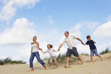 Full length of a happy family holding hands and running down sand dune on beach