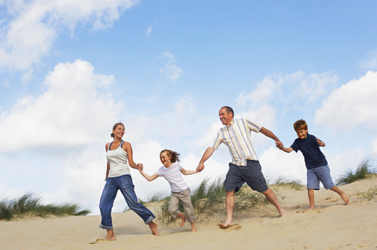 Full Length Of A Happy Family Holding Hands And Running Down Sand Dune On Beach