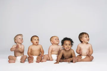 Fototapeten Row of multiethnic babies sitting side by side looking away isolated on gray background © moodboard