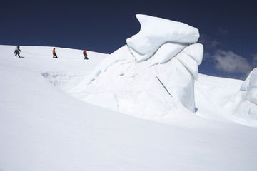 Fototapeta na wymiar Side view of three hikers walking past ice formation at a distance in snowy mountains